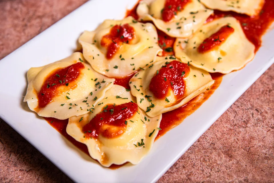 BookNoFees: Foto de ejemplo: Raviolis con salsa de tomate y hierbas en un plato blanco