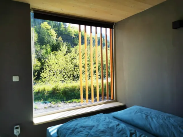 BookNoFees: alojamiento vacacional en Hieflau, Estiria, Austria – Habitación con ropa de cama azul y una gran ventana con persianas de madera con vista al bosque