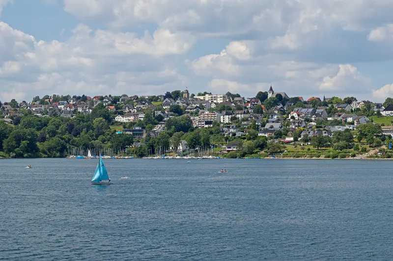 BookNoFees: Langscheid, a orillas del lago Sorpesee, cerca de Sundern: el pueblo a orillas del lago, elevado sobre el agua, con un velero al frente