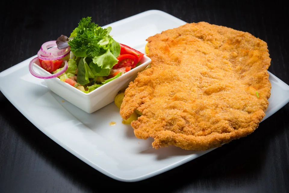 BookNoFees: Foto de ejemplo: Schnitzel empanado con una ensalada de acompañamiento en un plato blanco