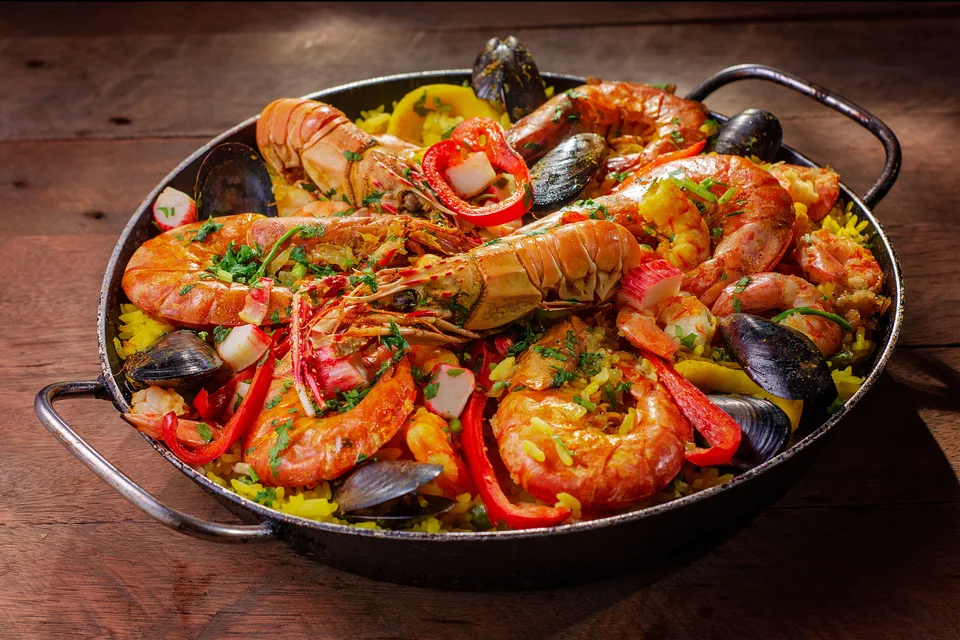 BookNoFees: Foto de ejemplo: Una paella de marisco con gambas y pimientos rojos por encima.
